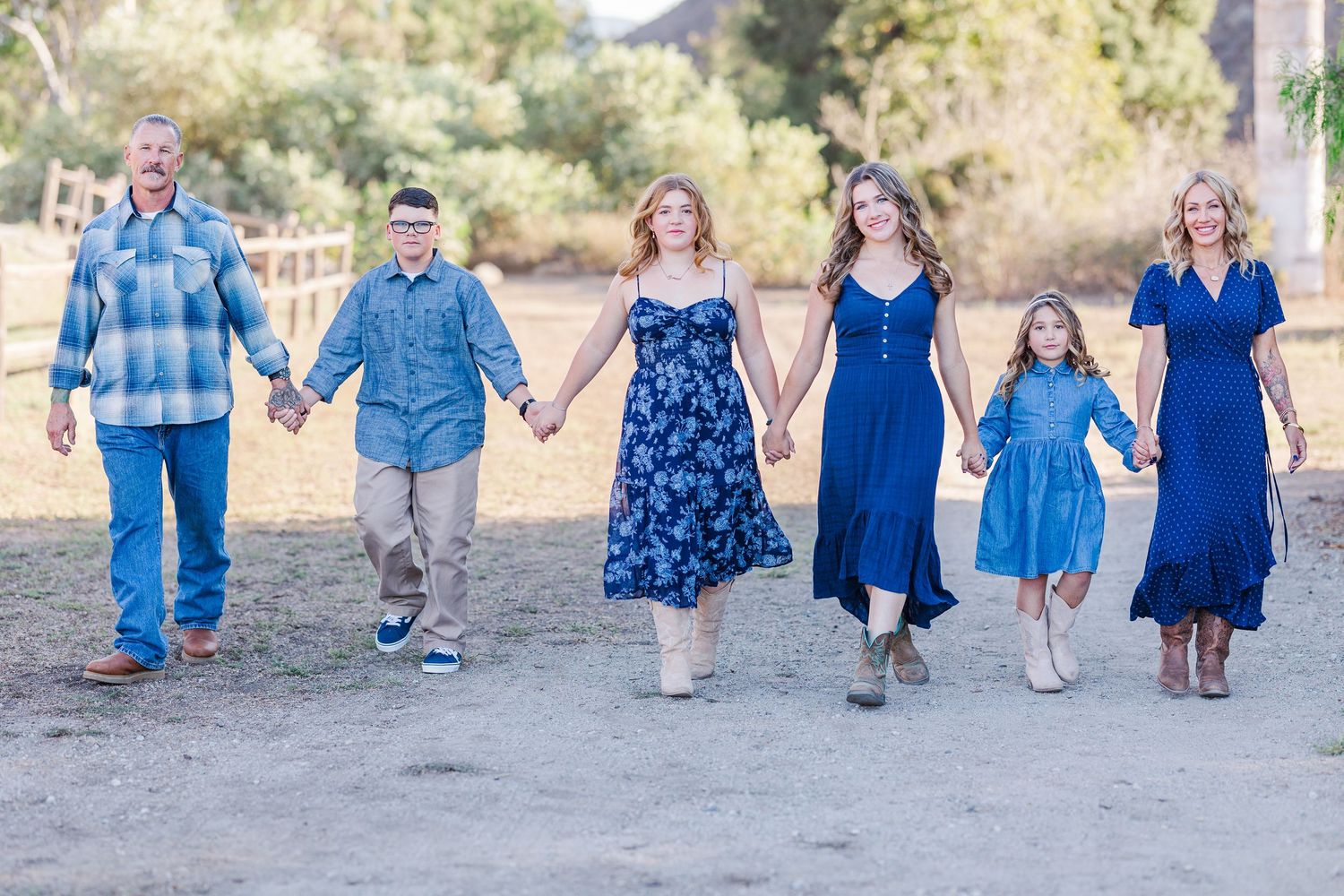 Family group wearing coordinated blue and denim outfits walking together outdoors in a natural setting.