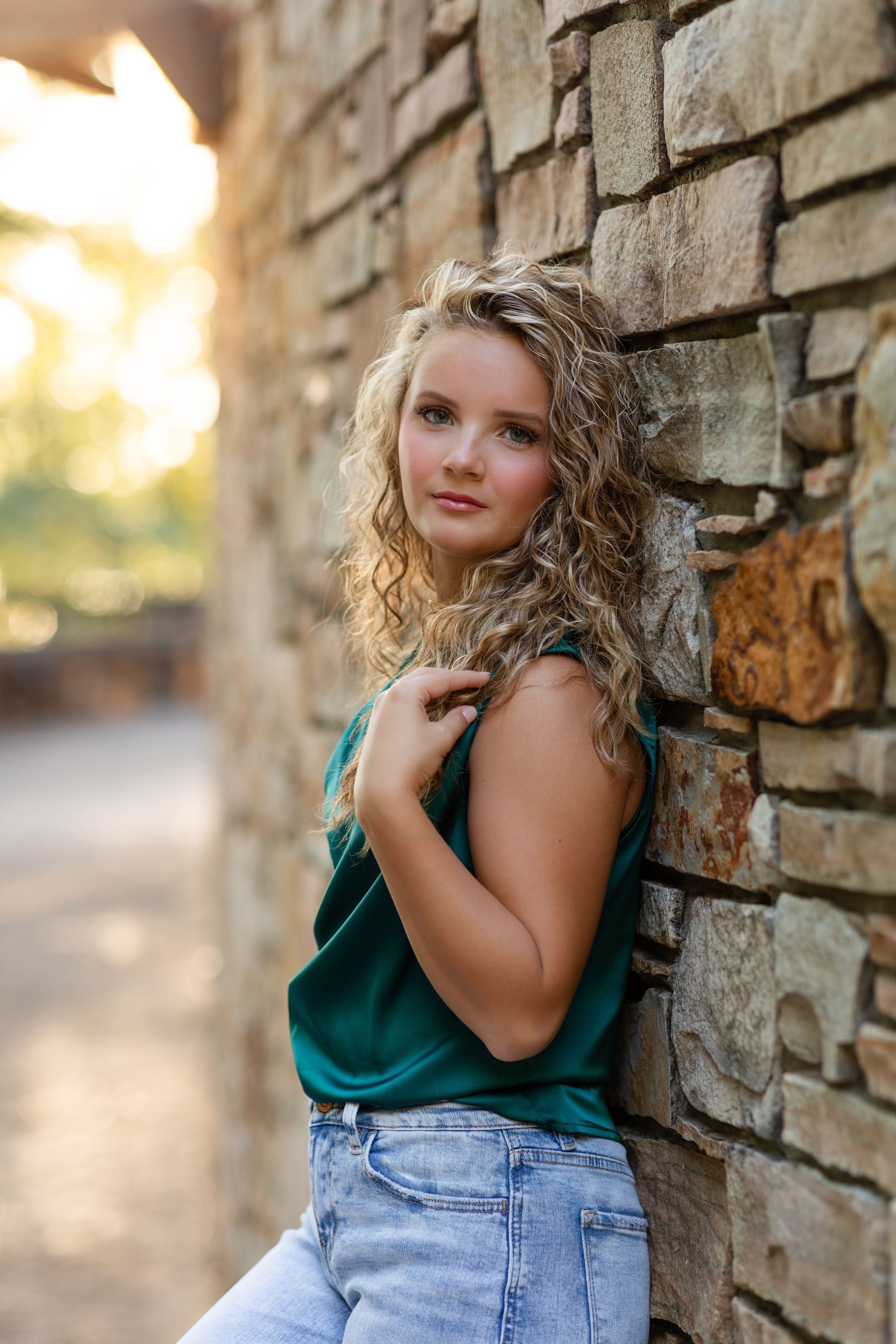Casual portrait against stone wall wearing green top and denim.