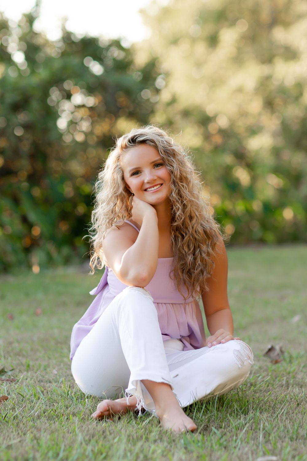 A person in a pink and white outfit sits casually on grass during a sunny outdoor photo session.