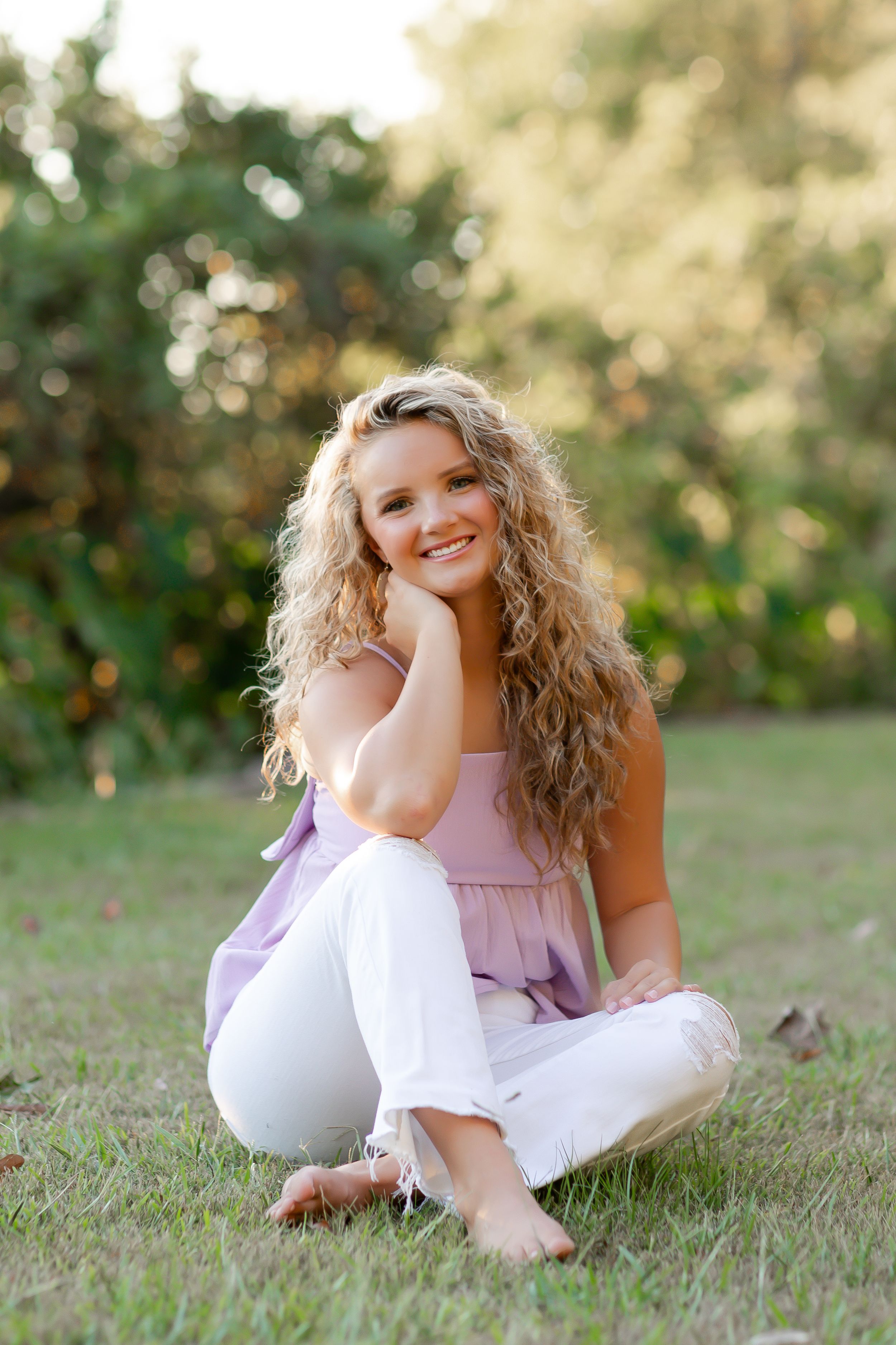 A person in a pink and white outfit sits casually on grass during a sunny outdoor photo session.