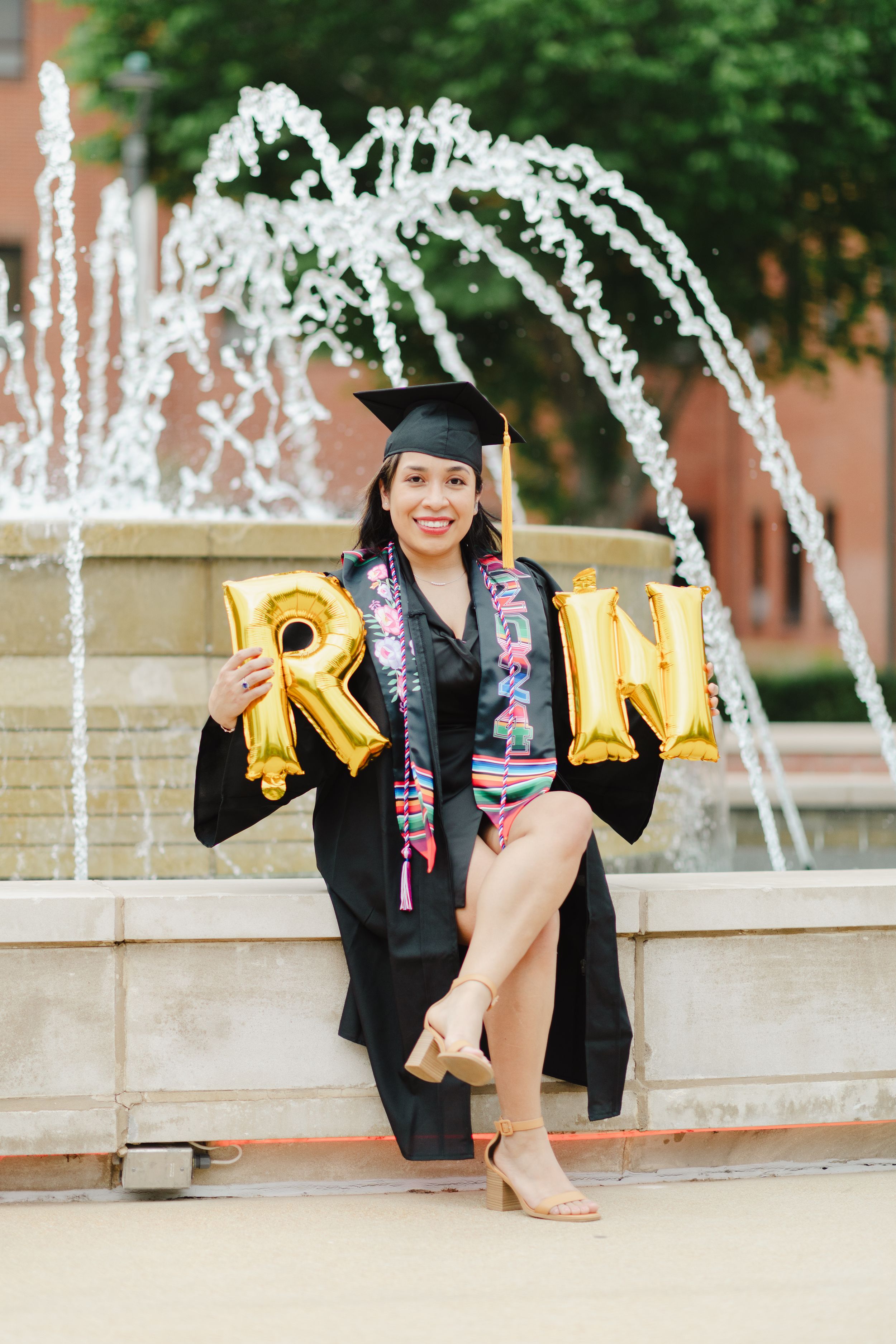 Graduation photos with gold balloon letters and decorative fountain in the background.