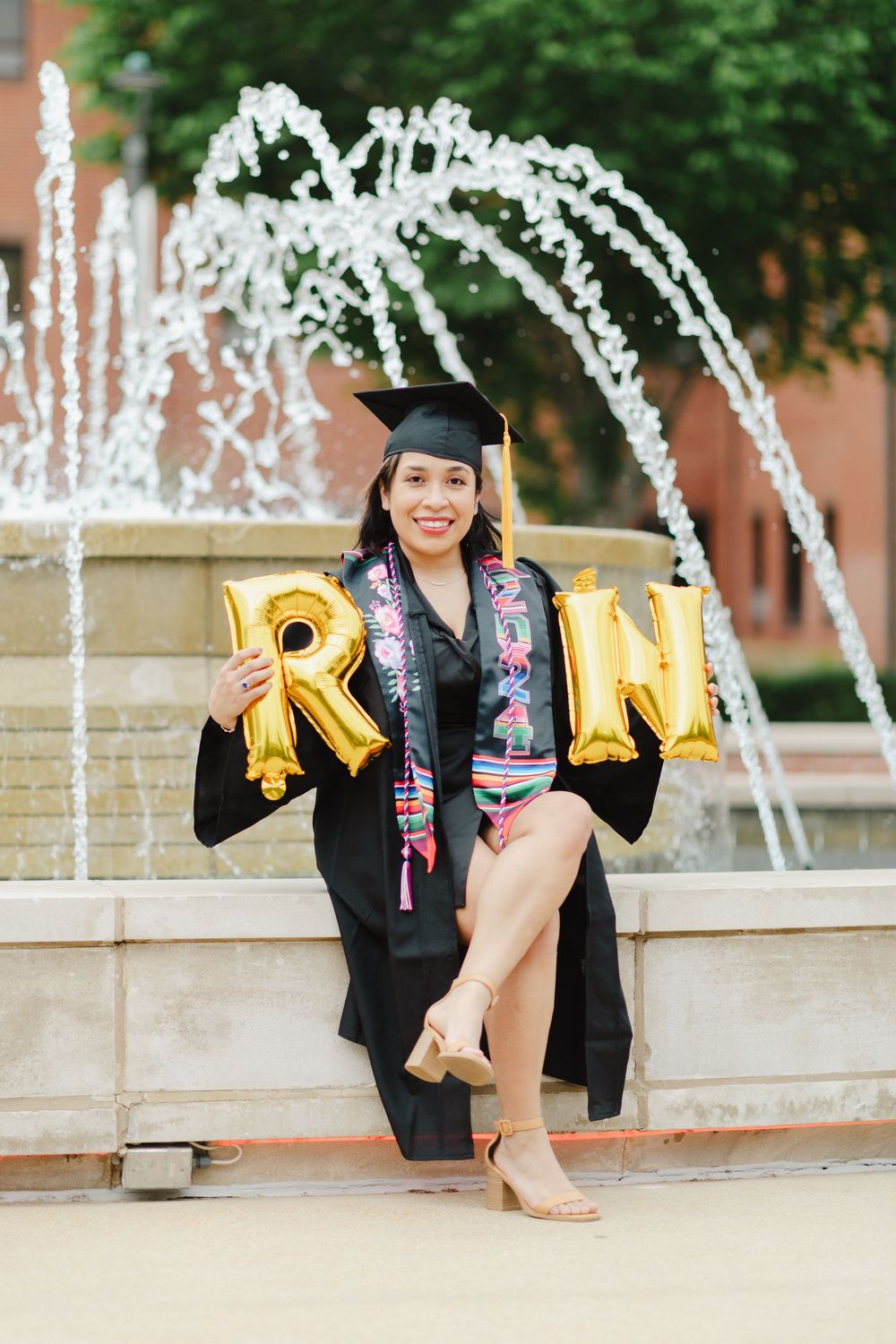 Graduation photos with gold balloon letters and decorative fountain in the background.
