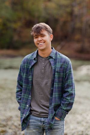 A person wearing a plaid flannel shirt and grey henley poses outdoors in a casual autumn photoshoot.