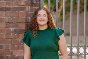 Portrait against brick wall wearing emerald green top with ruffled sleeves.