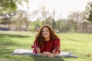 Outdoor portrait session in burgundy top laying on grass at sunset.