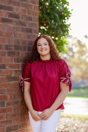 Portrait against brick wall wearing burgundy top with tied sleeves.