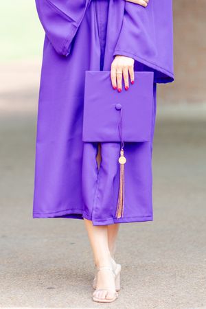 Close-up of purple graduation gown with gold tassel and white shoes.