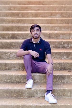 A casual portrait of someone sitting on concrete steps wearing purple pants and white sneakers.