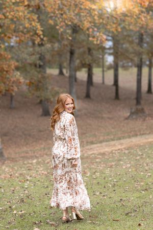A floral dress twirls gracefully among autumn trees in a park setting.