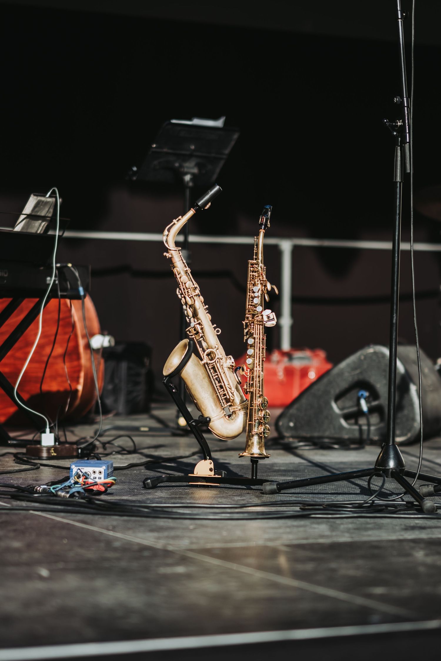 Multiple saxophones rest on a dark stage floor with microphones and equipment visible in dramatic lighting.