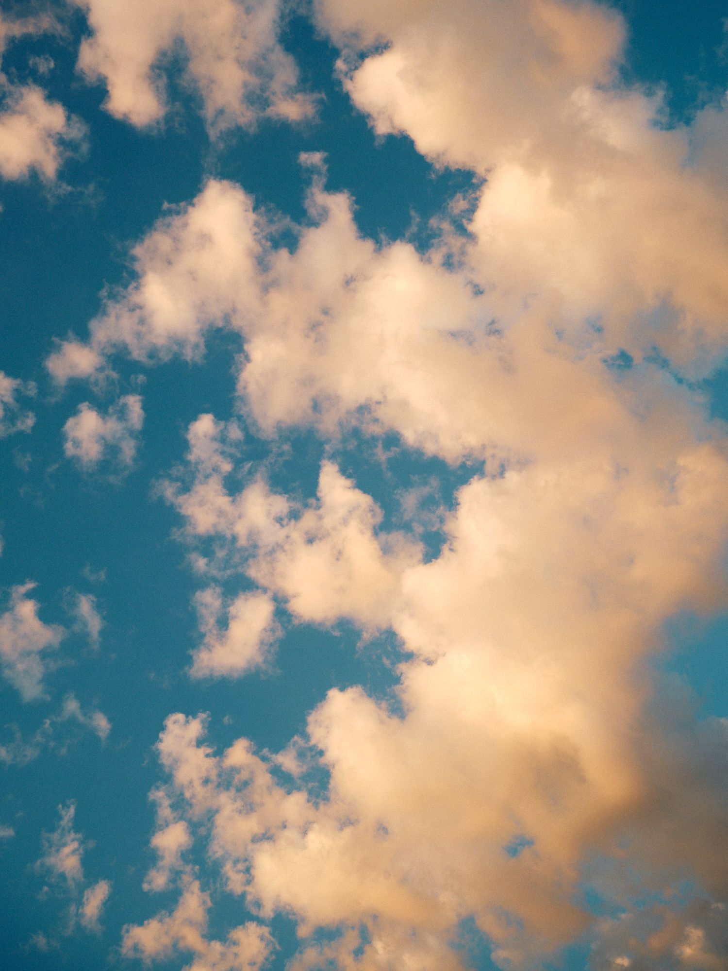 Dreamy golden clouds float across a vibrant turquoise blue sky in a peaceful atmospheric scene.