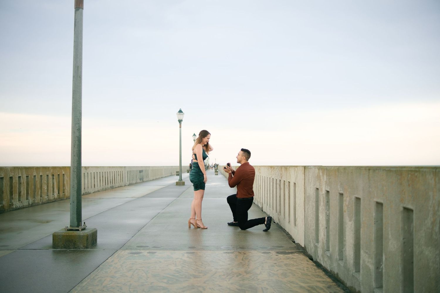 Long concrete pier extends over water with silhouettes of people walking at dusk.