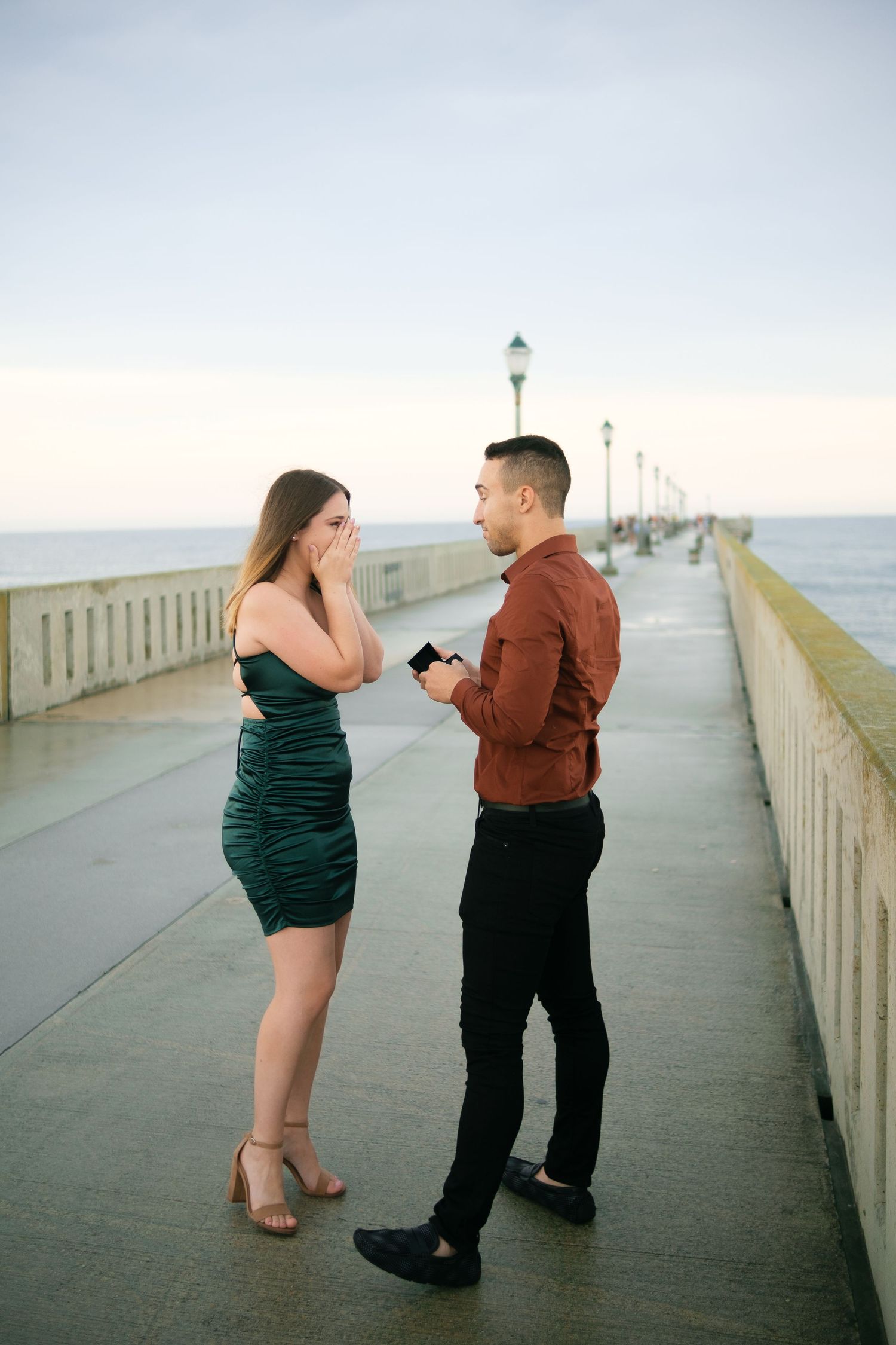 A couple shares tender moments while walking along a misty oceanfront pier with lampposts in the background.