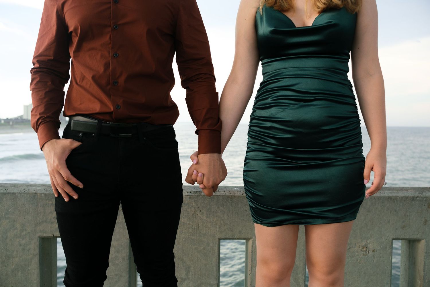 Couple standing together by ocean wearing brown and green outfits.