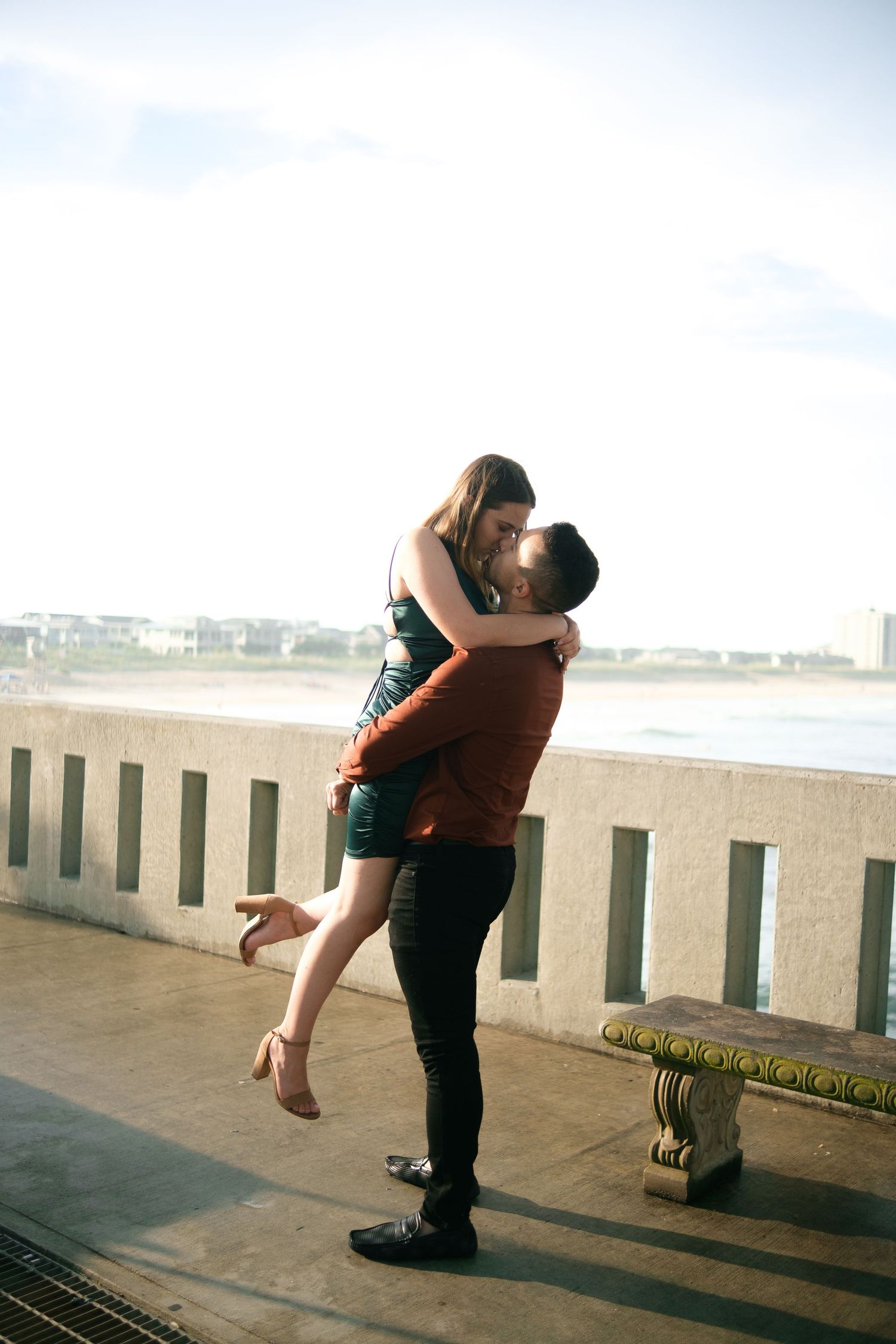 A couple embraces passionately on a concrete pier with ocean views in the background.