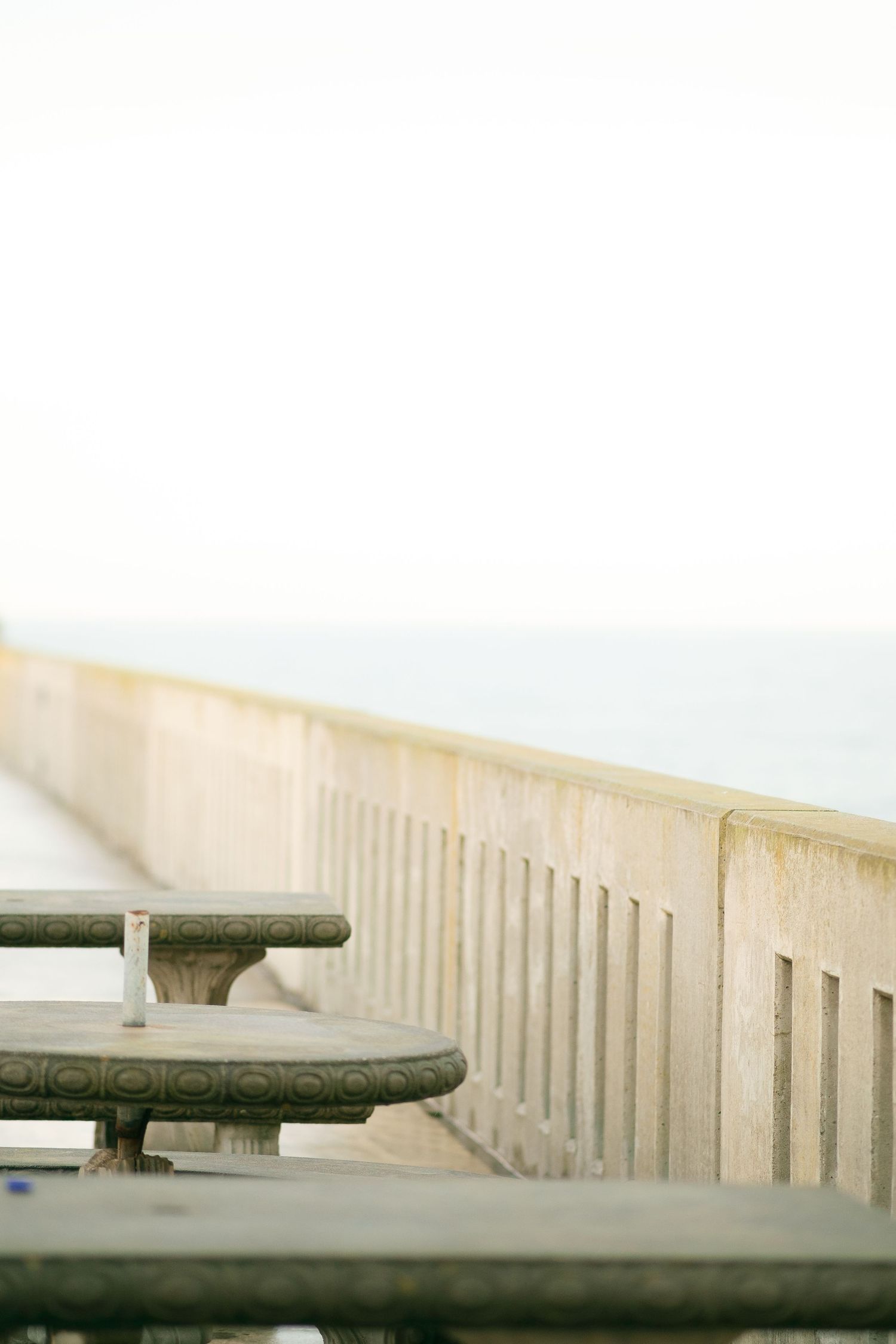 A minimalist seaside boardwalk with wooden benches and white railing stretching into the foggy distance.