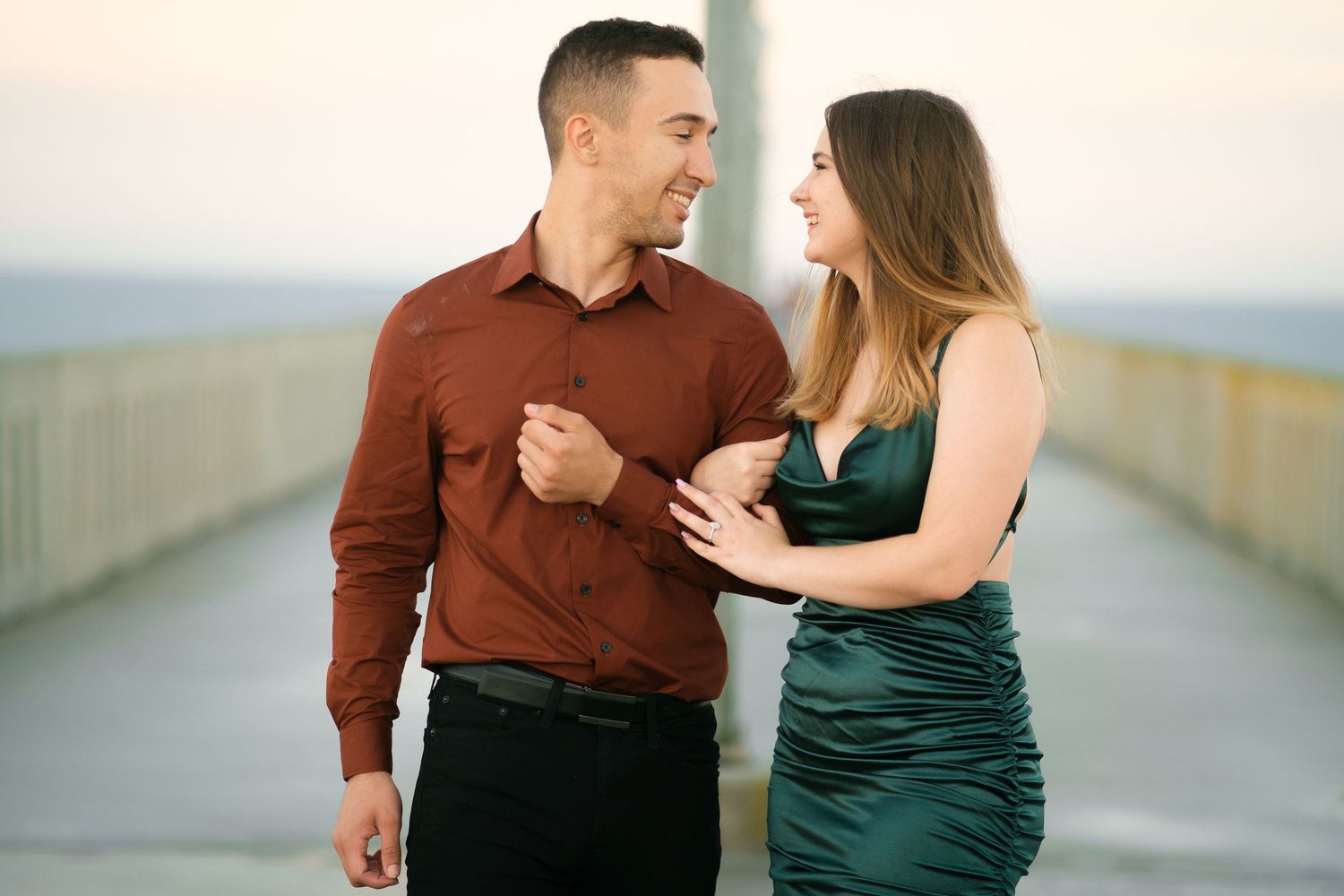 A couple in formal attire poses together on an outdoor walkway during a photoshoot.