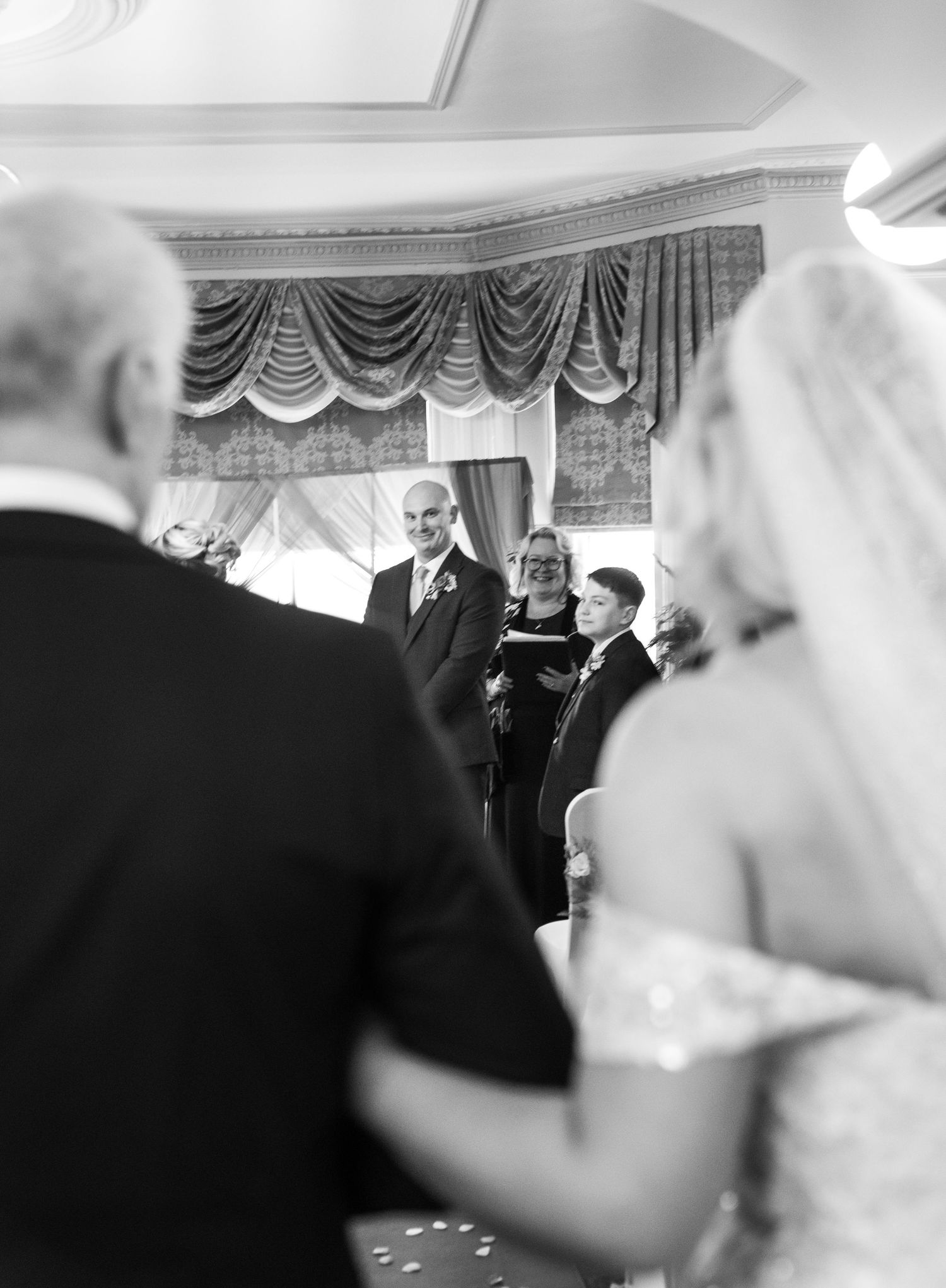 Black and white sequence of wedding ceremony moments showing guests and decorative drapes in an elegant venue.