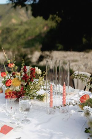 Wedding table setting with coral floral arrangements and tall glass centerpieces on white linen.