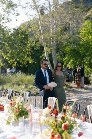 Event staff prepare an elegant outdoor table setting with floral arrangements and glassware.