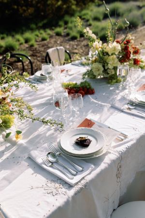 Elegant place setting with white linens and floral centerpieces in outdoor garden setting.