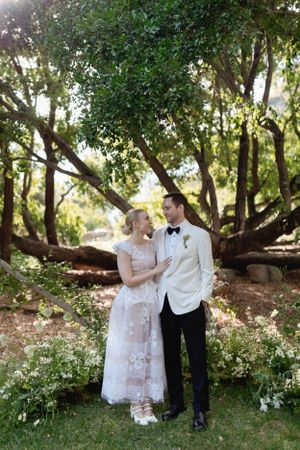 Wedding couple posing together under trees in a garden setting.