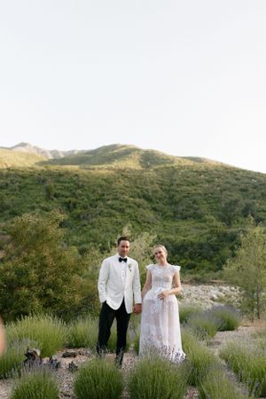 Couple in formal attire standing against scenic mountain landscape.