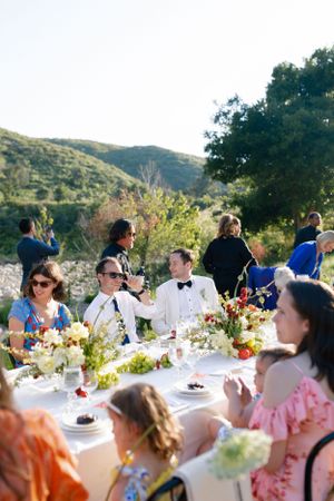 Elegant outdoor wedding reception table setting with floral centerpieces against mountainous backdrop.
