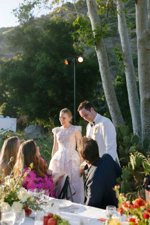 An outdoor wedding reception under trees with string lights and floral table decorations.