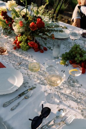 Elegant outdoor table setting with white lace runner, wine glasses and floral centerpiece.