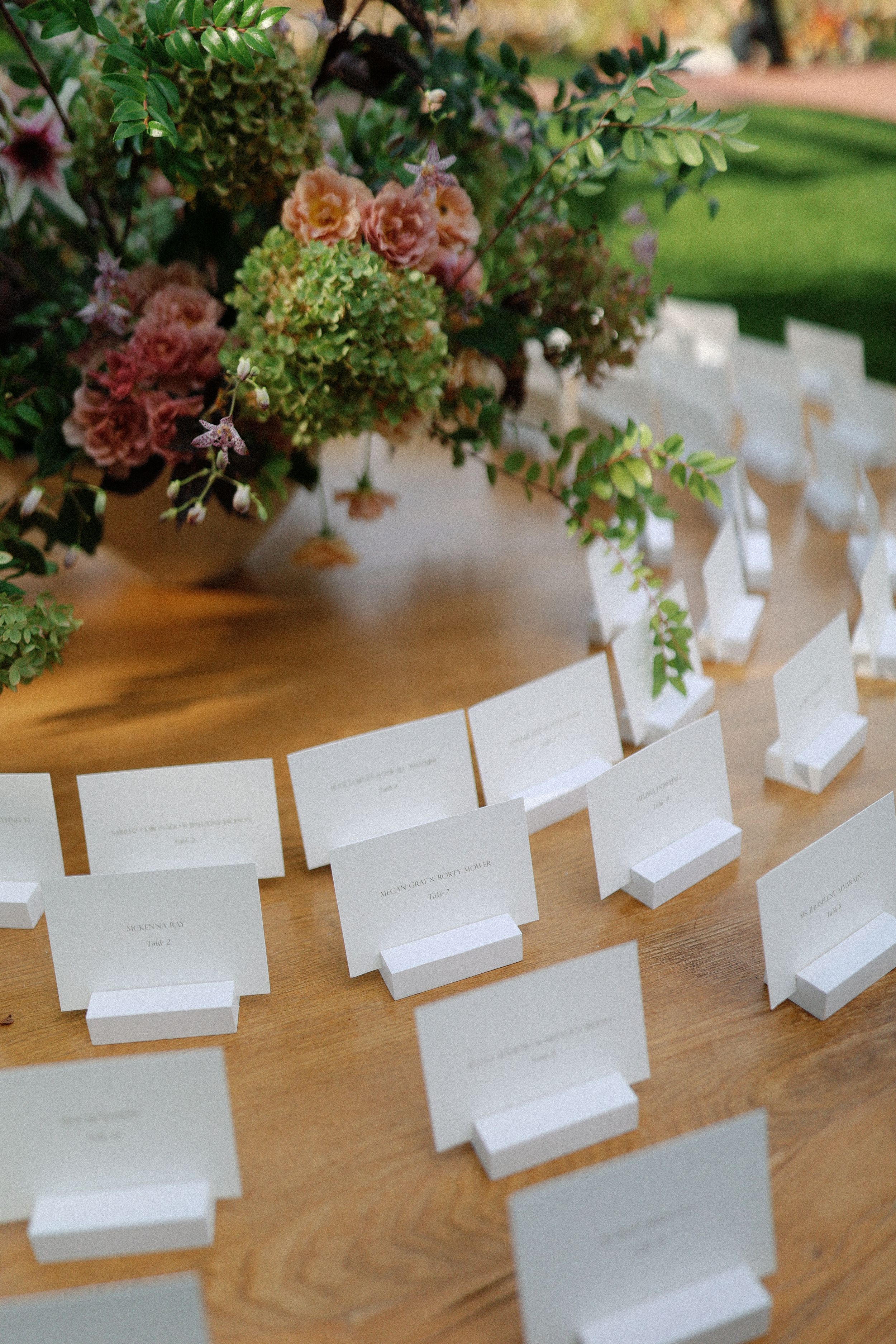 Wedding place cards arranged on a wooden table with floral decorations above.