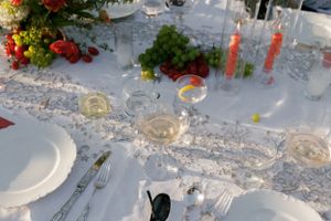 Close-up of formal place setting with lace runner, wine glasses and red floral arrangements.
