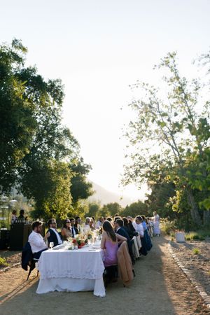 Guests seated at a long outdoor dining table during sunset with mountain views.