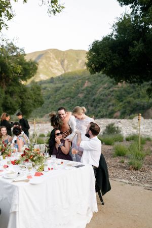 Wedding guests enjoying dinner at outdoor table with mountain backdrop.