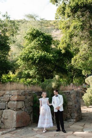 Wedding couple standing against stone wall backdrop in natural setting.