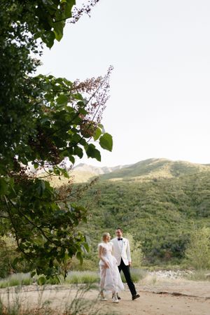A couple walks along a mountainside path surrounded by lush greenery.