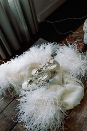 White feathered bridal shoes with crystal details on wooden floor.