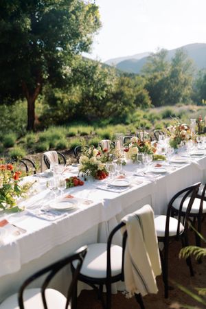 Elegant outdoor wedding table setting with white linens and floral centerpieces against a mountain backdrop.