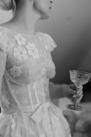 Close-up of a delicate white lace wedding dress bodice and crystal champagne glass.