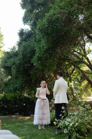 A couple shares an intimate moment during their garden wedding ceremony under tall trees.