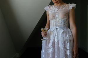 Close-up detail of a delicate white lace wedding dress with champagne glass.