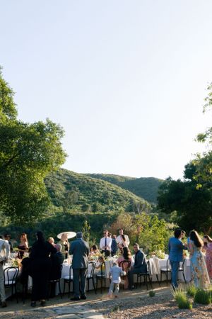 Outdoor wedding reception with mountain views and guests gathered at long tables.