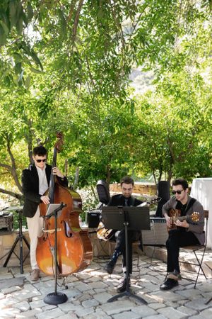 A three-piece band performs with upright bass, piano and guitar at an outdoor event.