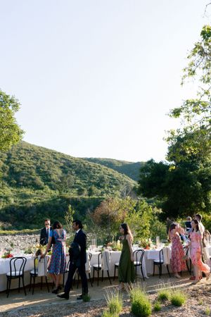 Elegant outdoor wedding reception with guests mingling around white-clothed tables against a mountain backdrop.