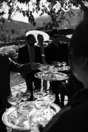 Black and white photo of champagne being served on trays at an outdoor reception.