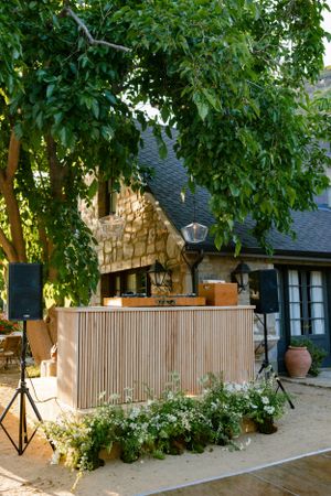 Outdoor bar setup with wooden panels and greenery against stone building.