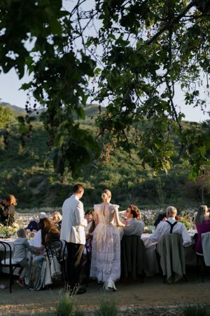 Guests enjoying an outdoor wedding reception under trees at dusk.