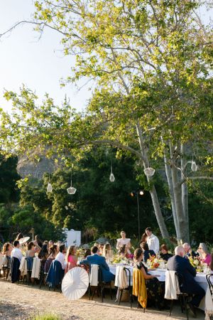 Outdoor wedding reception with hanging glass decorations and tables set beneath tall trees.