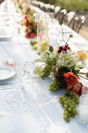 An elegant table setting with fresh flowers, grapes, and glassware for a wedding reception.