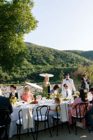 Guests dining at an outdoor reception table with parasols and mountain views.